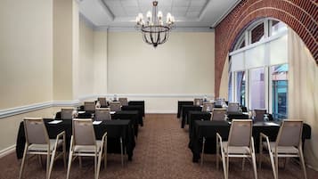 Uma sala de conferências com mesas, cadeiras, um candelabro e uma parede de tijolos.