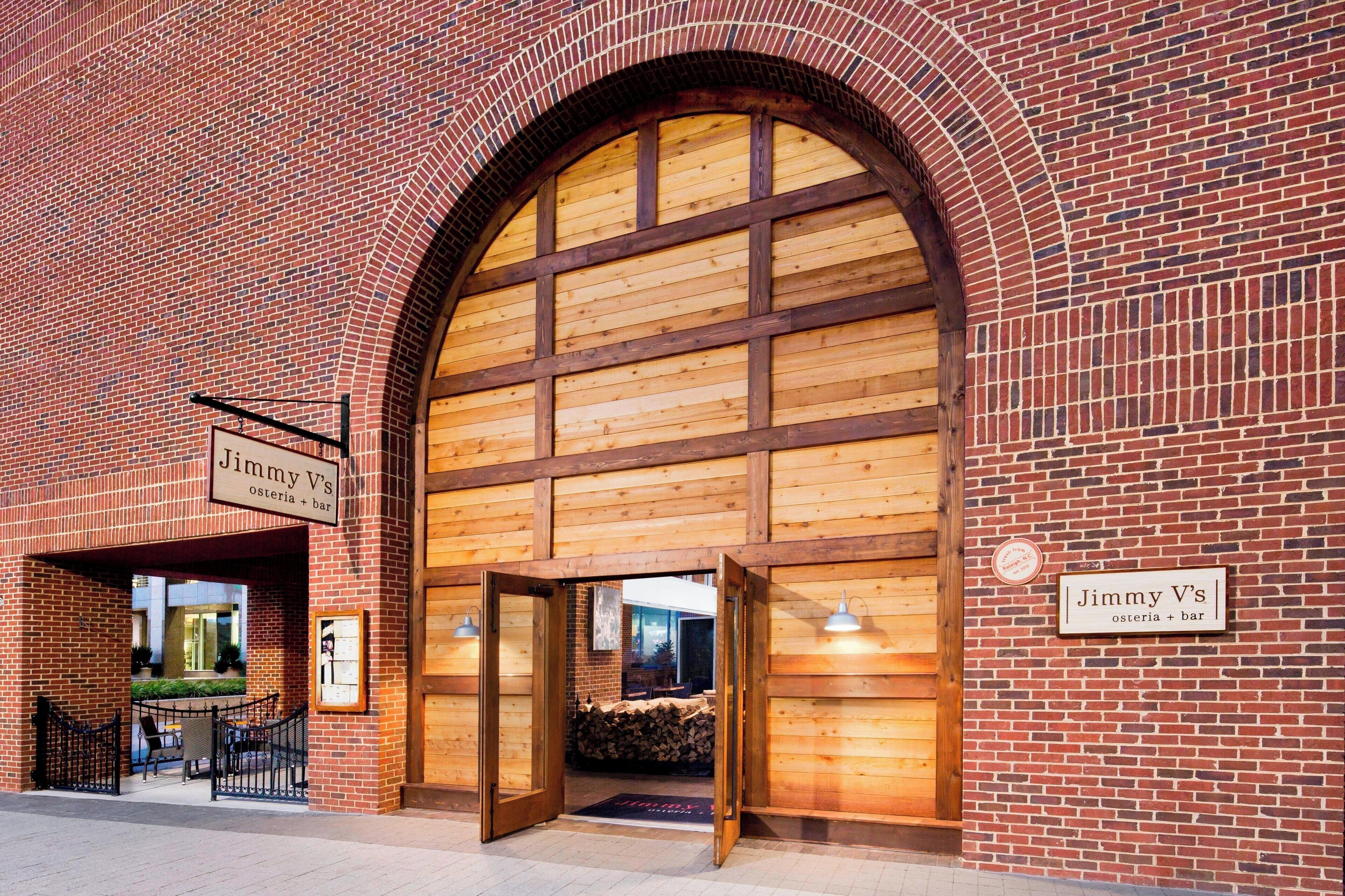 Un edificio de ladrillo con una entrada en arco y paneles de madera. Señales indican que es Jimmy V's, una osteria y bar.