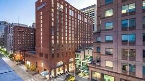 A multi-story hotel with a prominent Sheraton sign, a courtyard with seating, and a modern building adjacent to it.