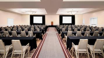 Una sala conferenze con file di tavoli e sedie, un corridoio rivestito di moquette e uno schermo per proiettore nella parte anteriore.