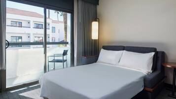 Een hotelkamer met een groot bed, een kleine tafel, een stoel en uitzicht op een gebouw door een glazen deur.