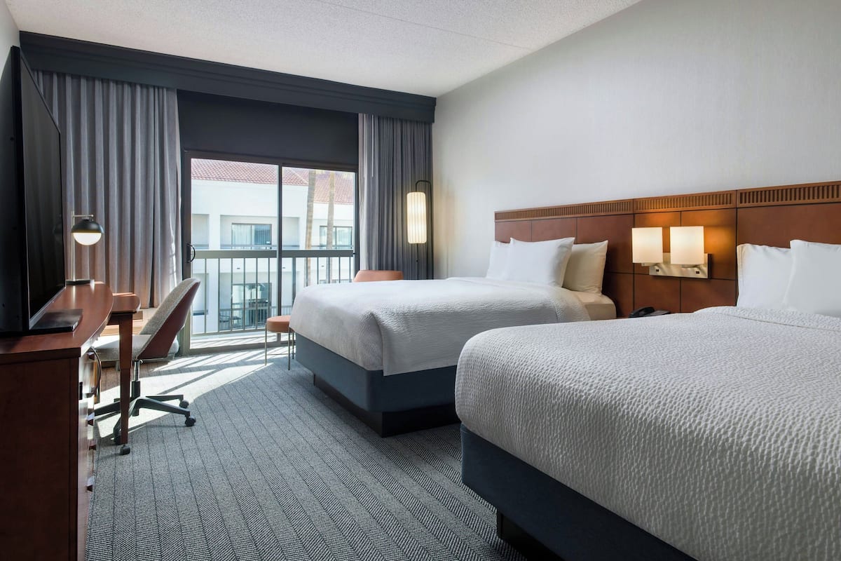 Une chambre d’hôtel avec deux lits, un bureau, une chaise et une grande fenêtre avec des rideaux.
