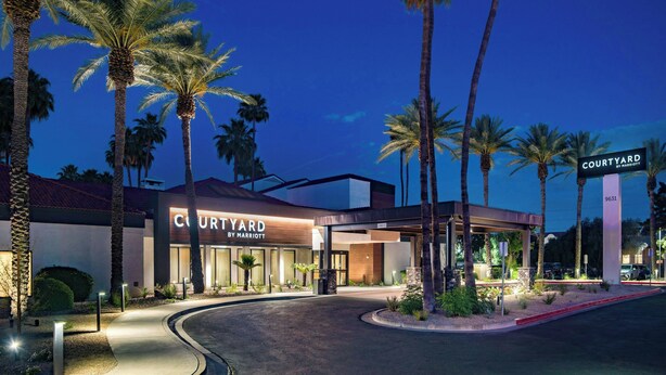 A Courtyard by Marriott hotel entrance with palm trees, a covered walkway, and a well-lit facade. - Courtyard Phoenix North by Marriott (Phoenix)