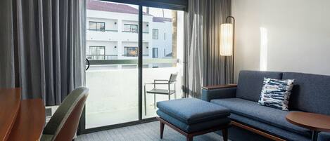 A hotel room with a sofa, a small table, a chair, and a large window with curtains.