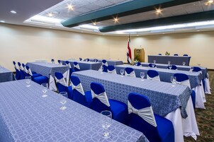 Una sala conferenze con tavoli apparecchiati per una riunione, sedie blu e un podio con una bandiera.