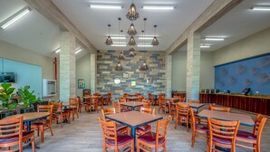 A spacious dining area with multiple tables and chairs, a patterned wall, and hanging pendant lights.
