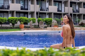 A woman sitting by a pool with a building in the background. - Irazu Hotel & Studios (San José)