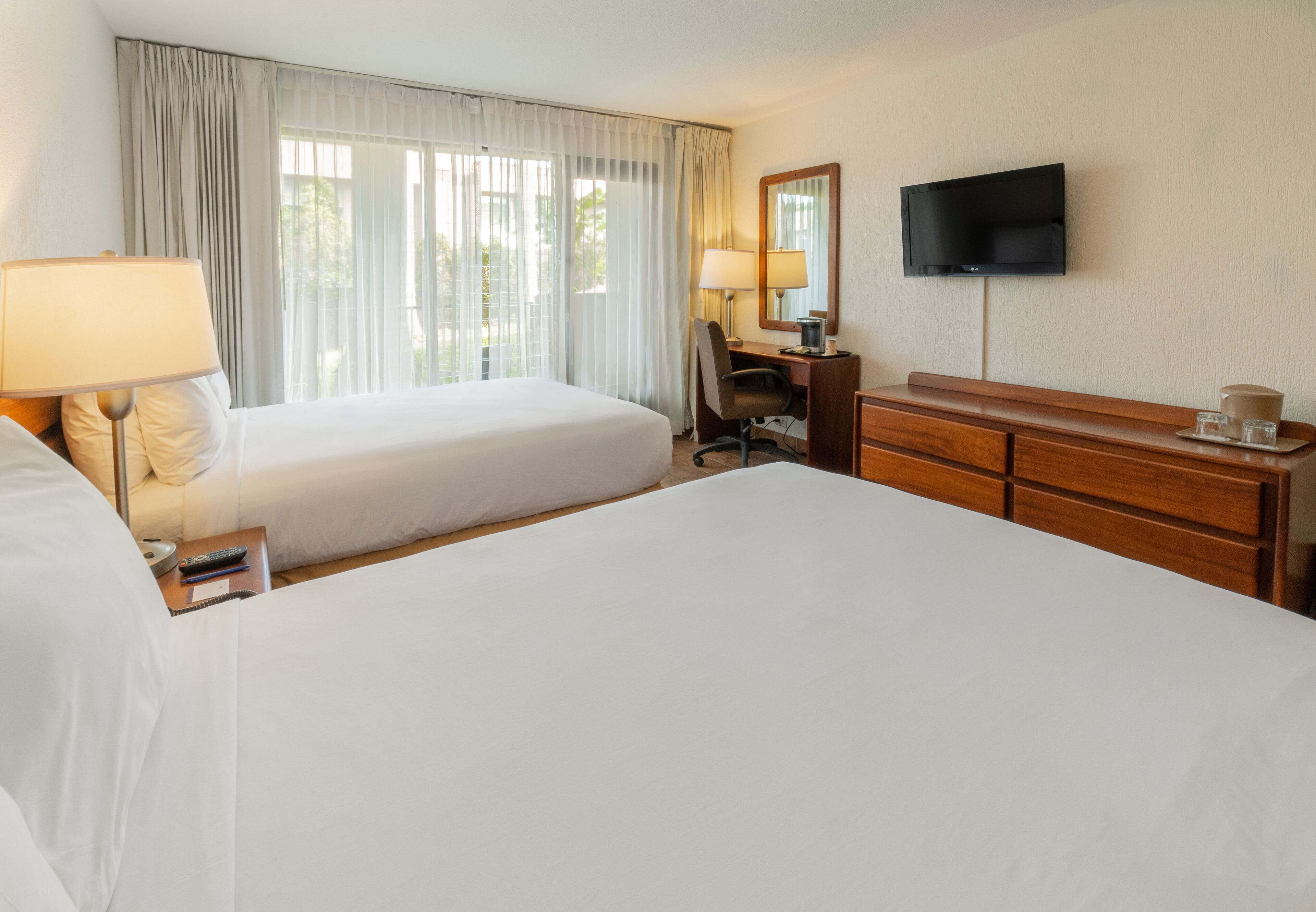 A hotel room with two beds, a desk, a chair, a TV, and a dresser.