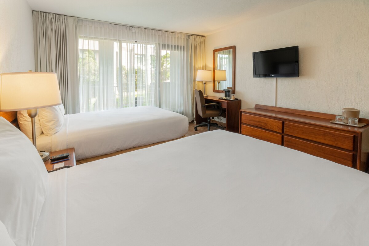 A hotel room with two beds, a desk, a chair, a TV, and a dresser.