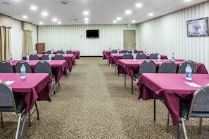 Una sala de conferencias con mesas y sillas, un televisor en la pared y una alfombra estampada.