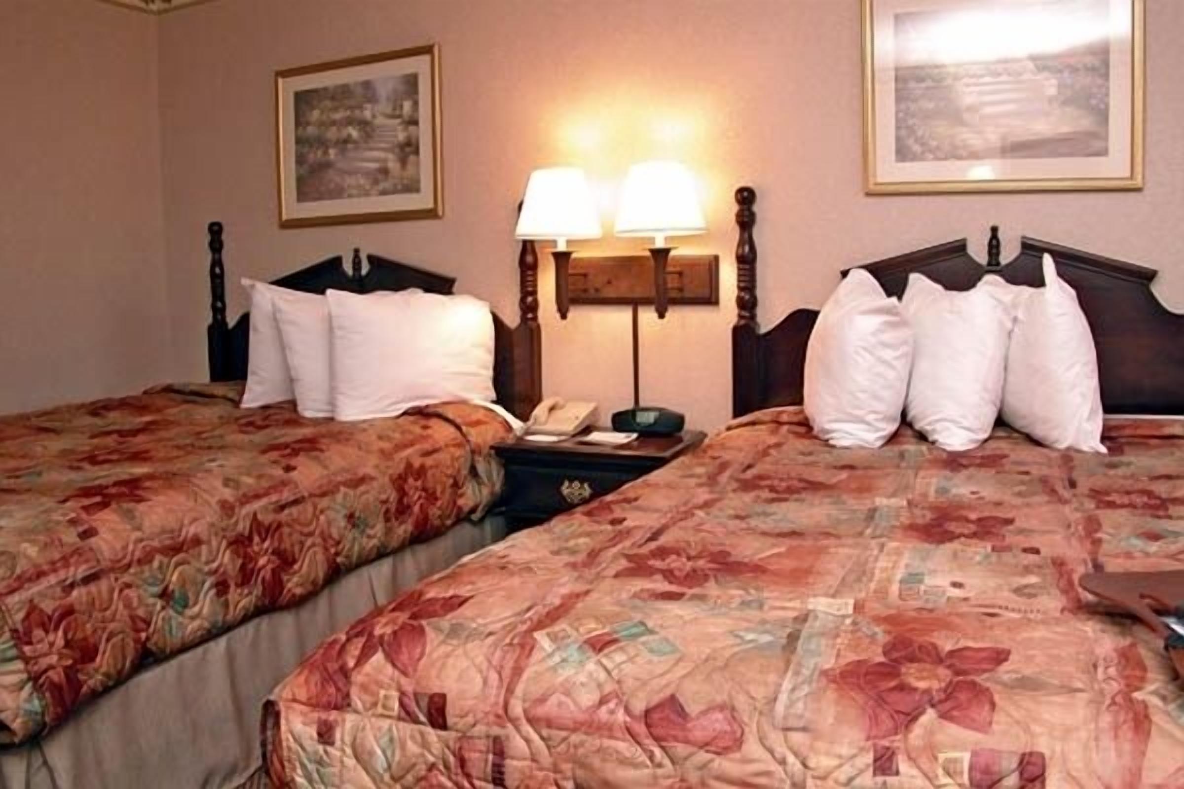 A hotel room with two beds, each with floral-patterned bedding, a nightstand with a lamp, and framed pictures on the walls.