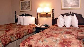 Habitación de hotel con dos camas, cada una con ropa de cama estampada con motivos florales, una mesita de noche con lámpara y cuadros en las paredes.