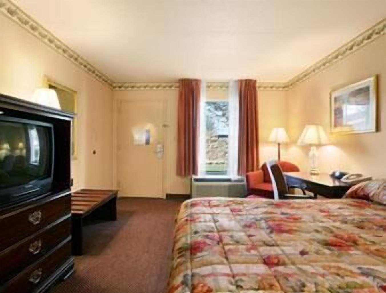 A hotel room with a bed, a television, a desk with a lamp, and a chair.