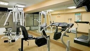 Un gimnasio con diversas máquinas de ejercicio, un espejo grande y un televisor montado en la pared.