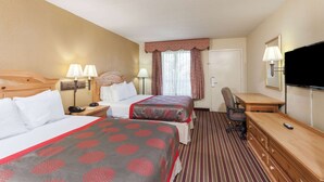 Habitación de hotel con dos camas, un escritorio, una silla, un televisor y un ventanal con cortinas.