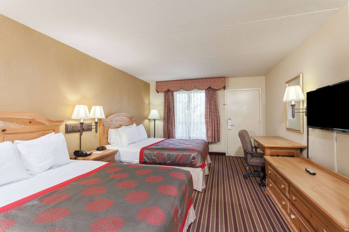 A hotel room with two beds, a desk, a chair, a TV, and a window with curtains.