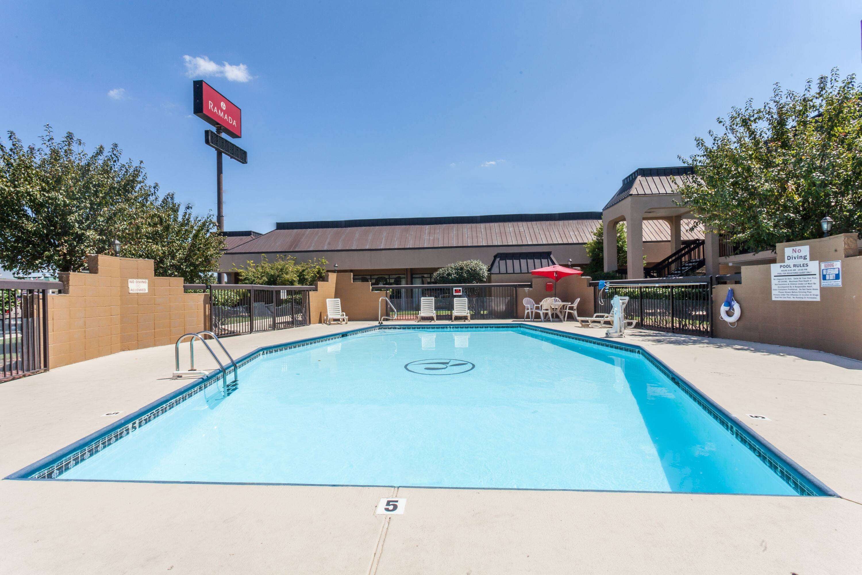 A swimming pool with lounge chairs and a sign for 'RAMADA' hotel.