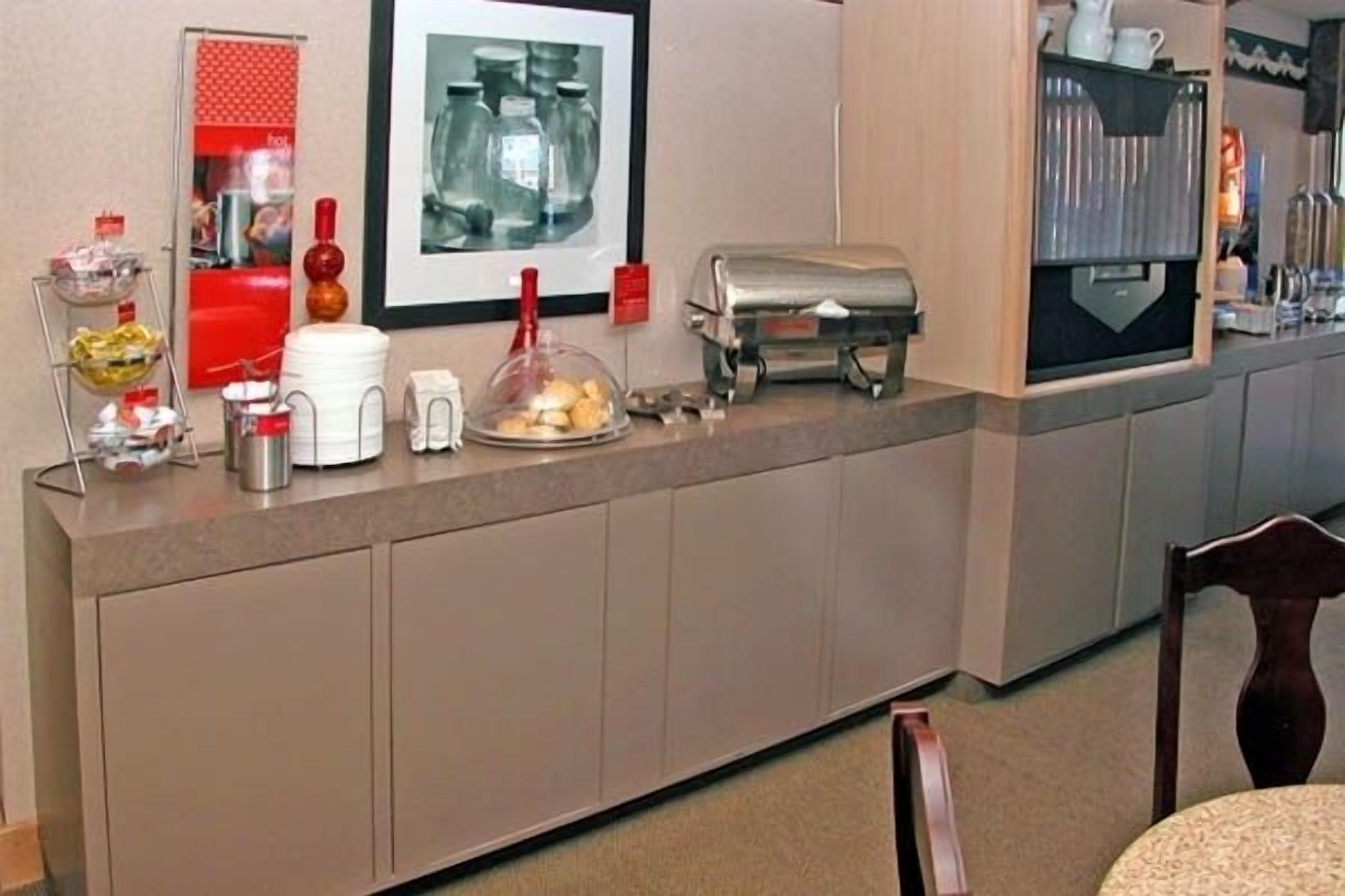 Un espace d’accueil d’hôtel comprenant un comptoir, une machine à café, un présentoir de nourriture et un tableau encadré au mur.