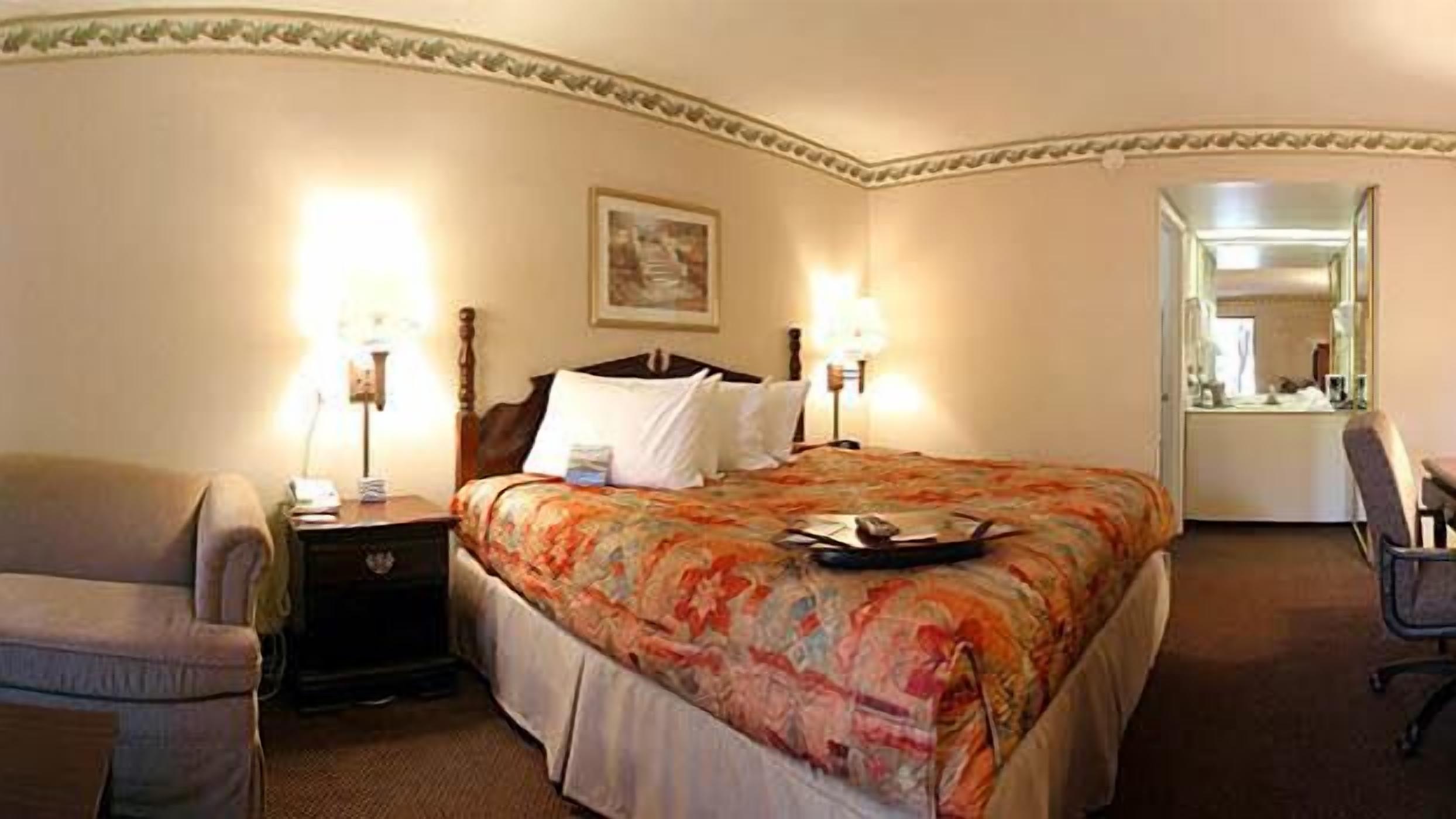 A hotel room with a bed, two bedside tables, a chair, a desk, and a mirror.