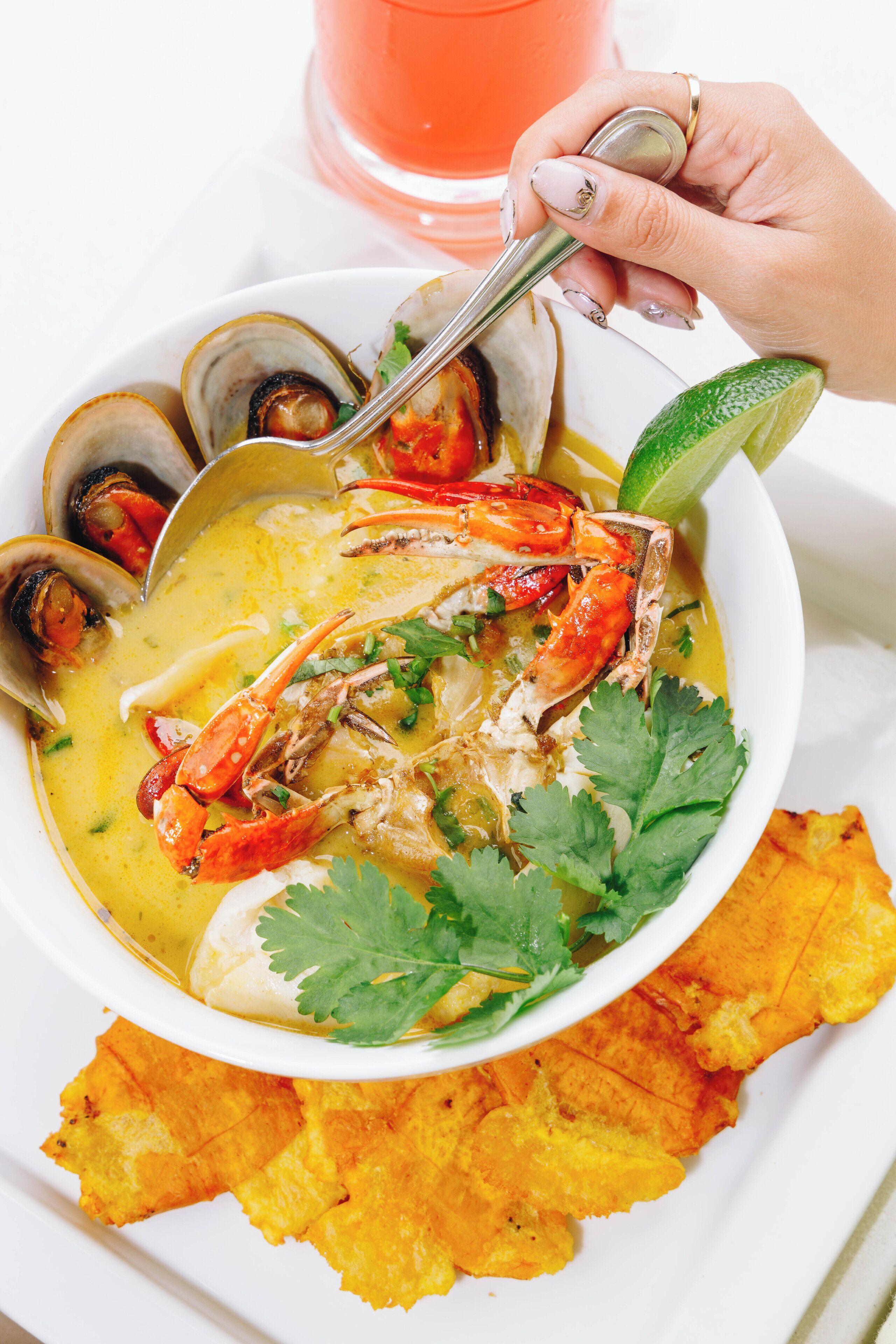 Un tazón de sopa de mariscos con cangrejo, almejas y lima, acompañado de plátanos fritos.
