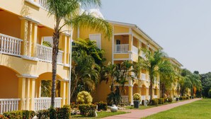Un edificio amarillo con balcones blancos y un paseo pavimentado.