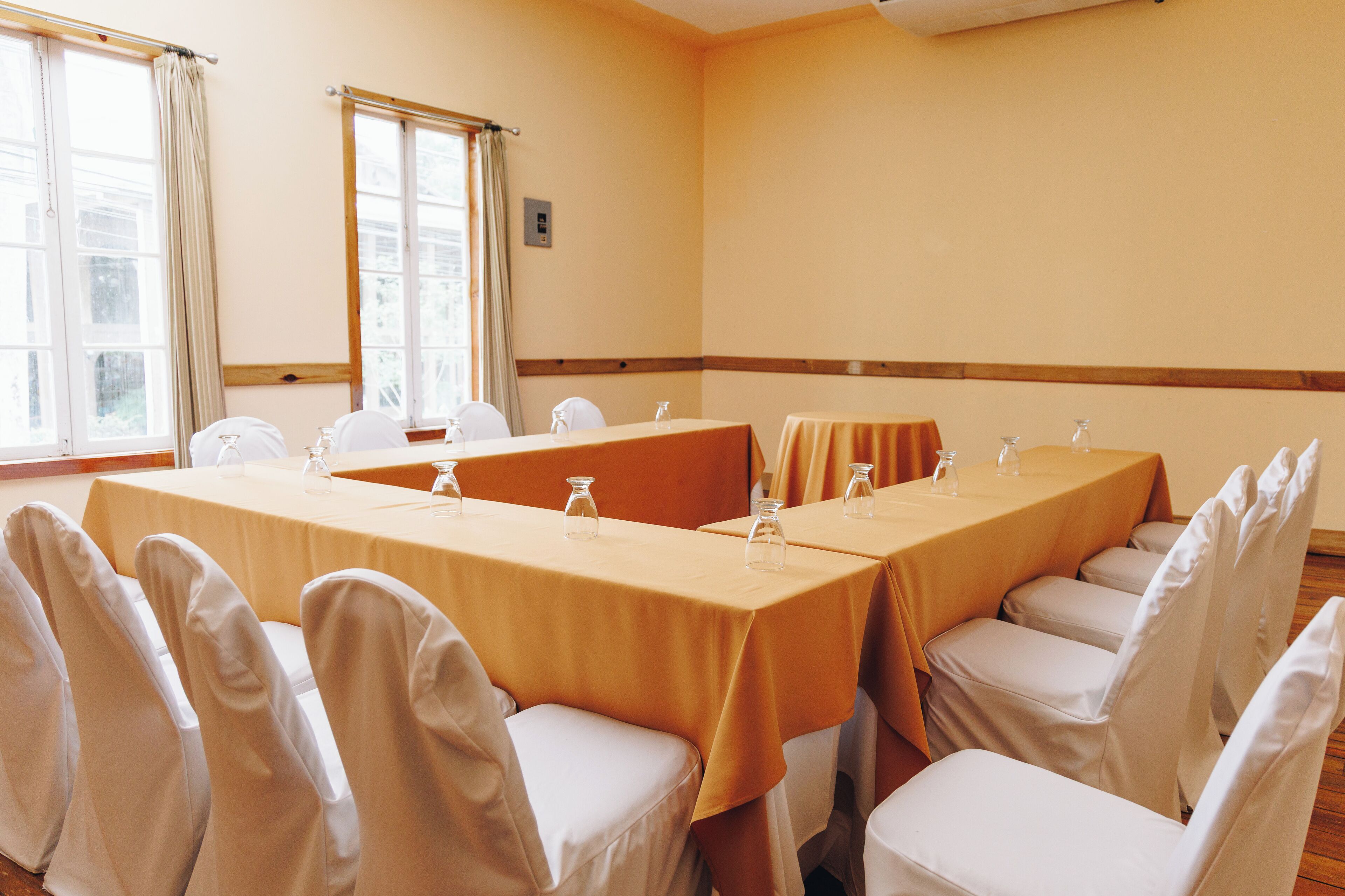 Un salón de conferencias con una larga mesa, sillas y un ventanal con cortinas.