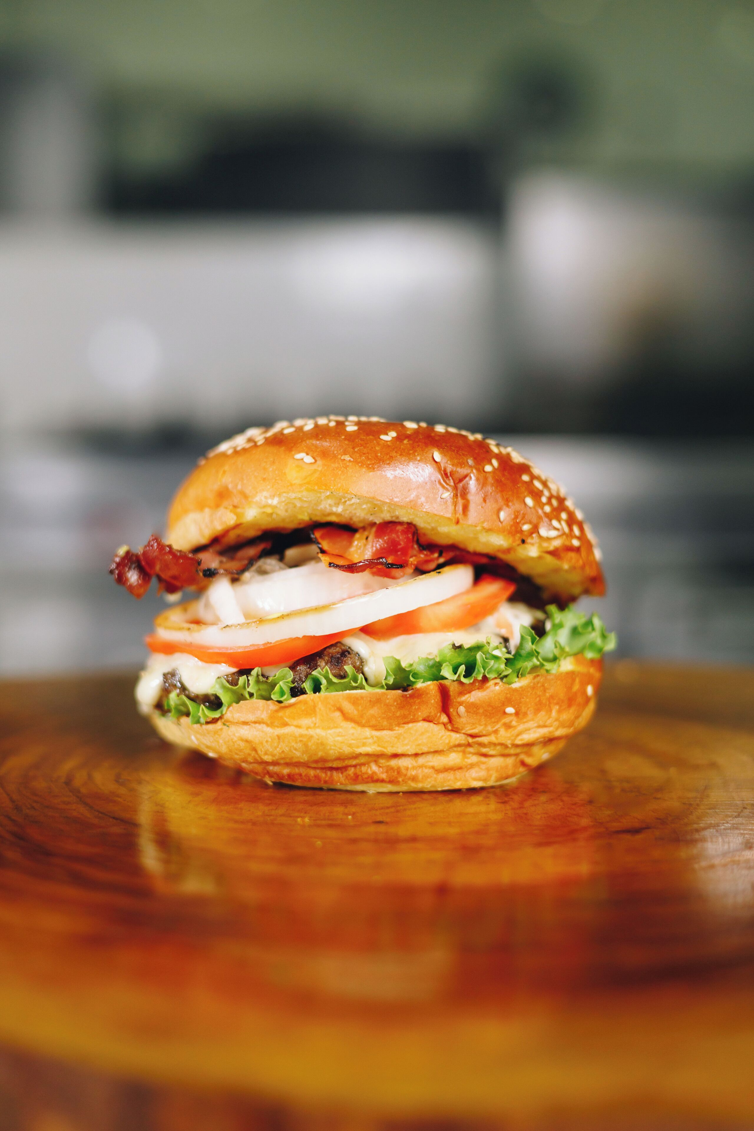 A burger with lettuce, tomato, and bacon on a sesame seed bun.