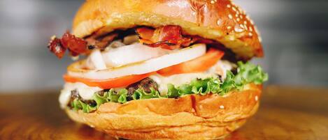 A burger with lettuce, tomato, and bacon on a sesame seed bun.