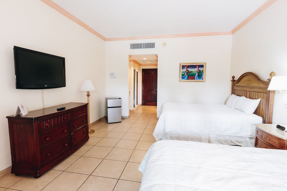 Quarto de hotel com duas camas, uma televisão, uma cômoda e um quadro na parede.