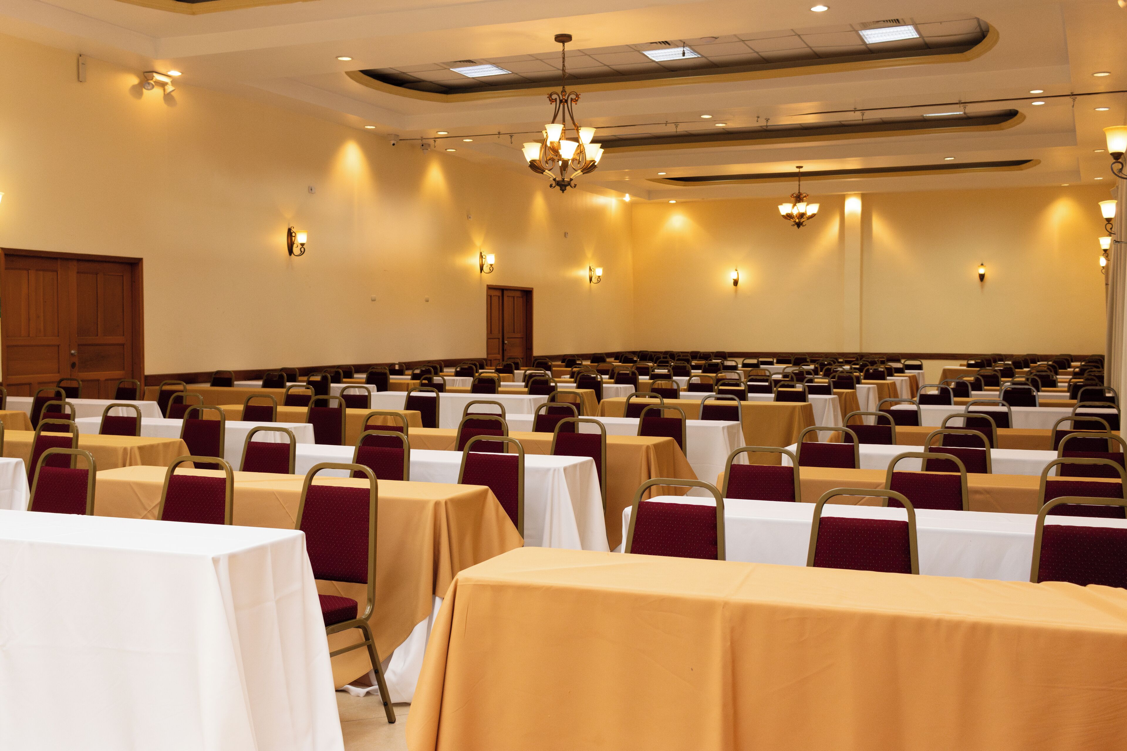 Une salle de conférence avec des rangées de tables et de chaises, agrémentée de lustres et d’appliques murales.