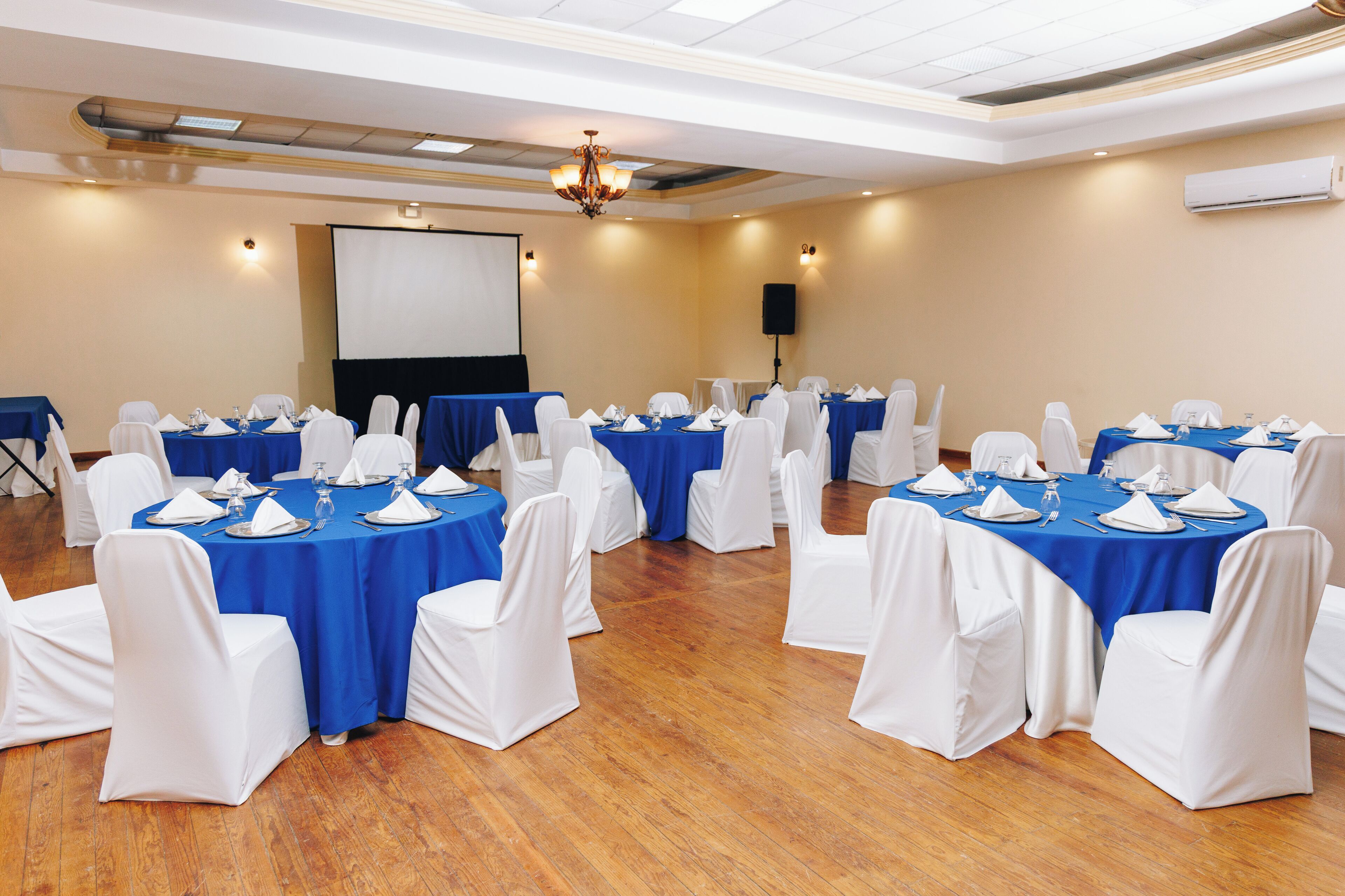 Un salón de conferencias con mesas redondas, sillas blancas y manteles azules.