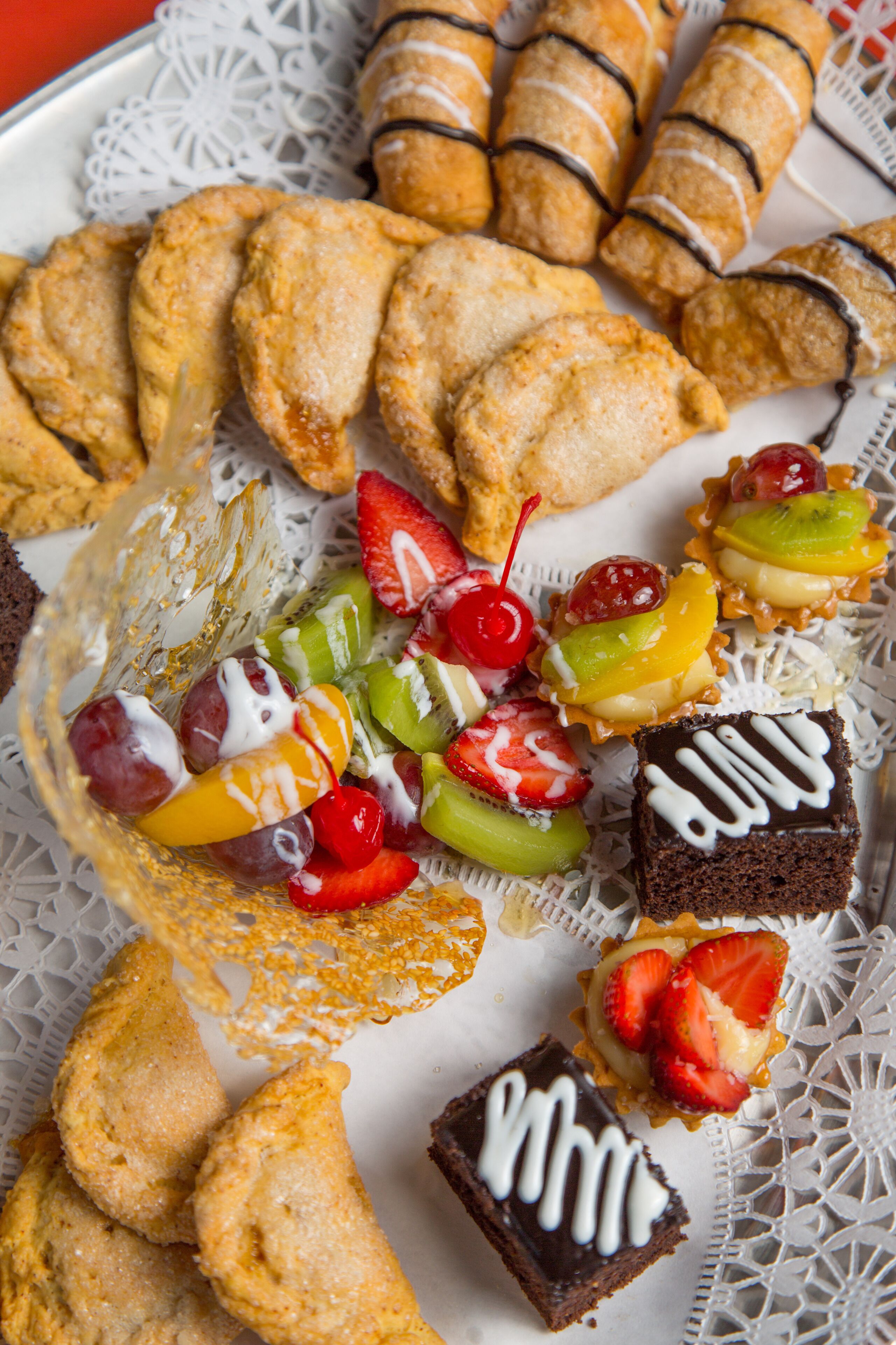 A tray of assorted pastries and desserts, including croissants, fruit-topped pastries, and a chocolate brownie with white icing.
