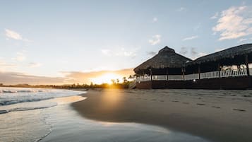 Une scène de plage avec une structure à toit de chaume et une terrasse en bois.