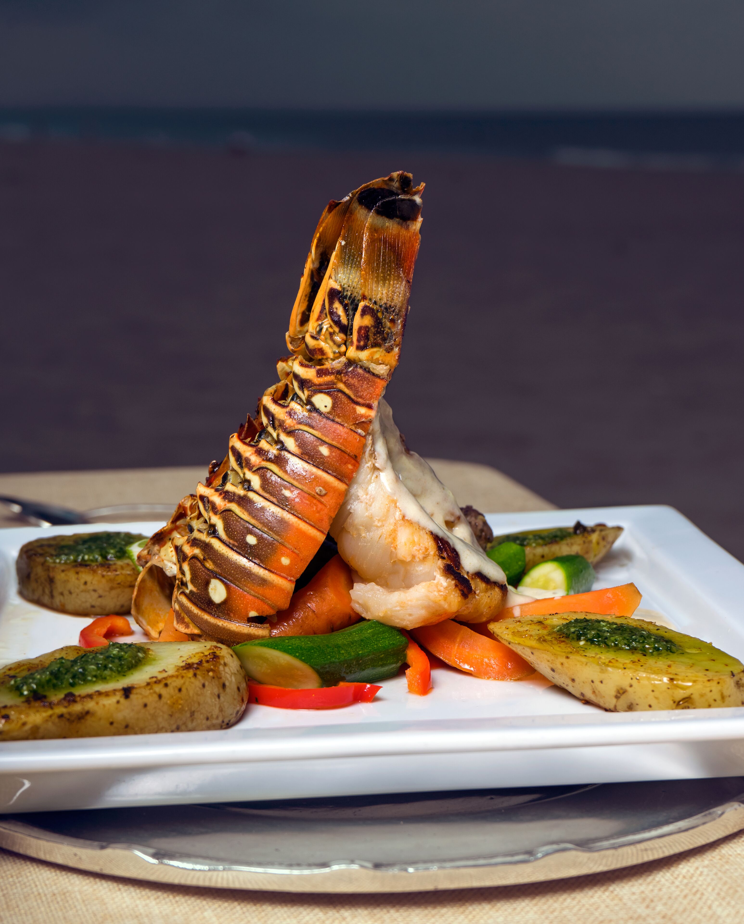 A lobster tail on a white plate with grilled vegetables.