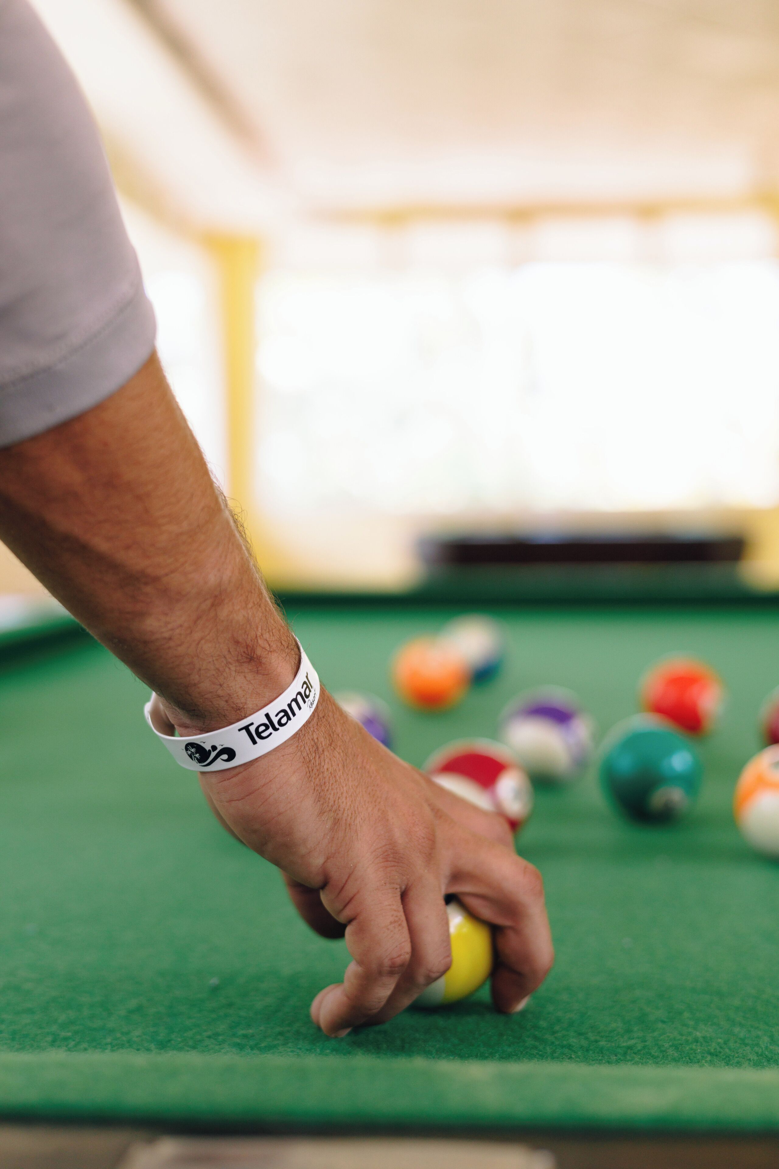 A hand holding a billiard ball on a green pool table.