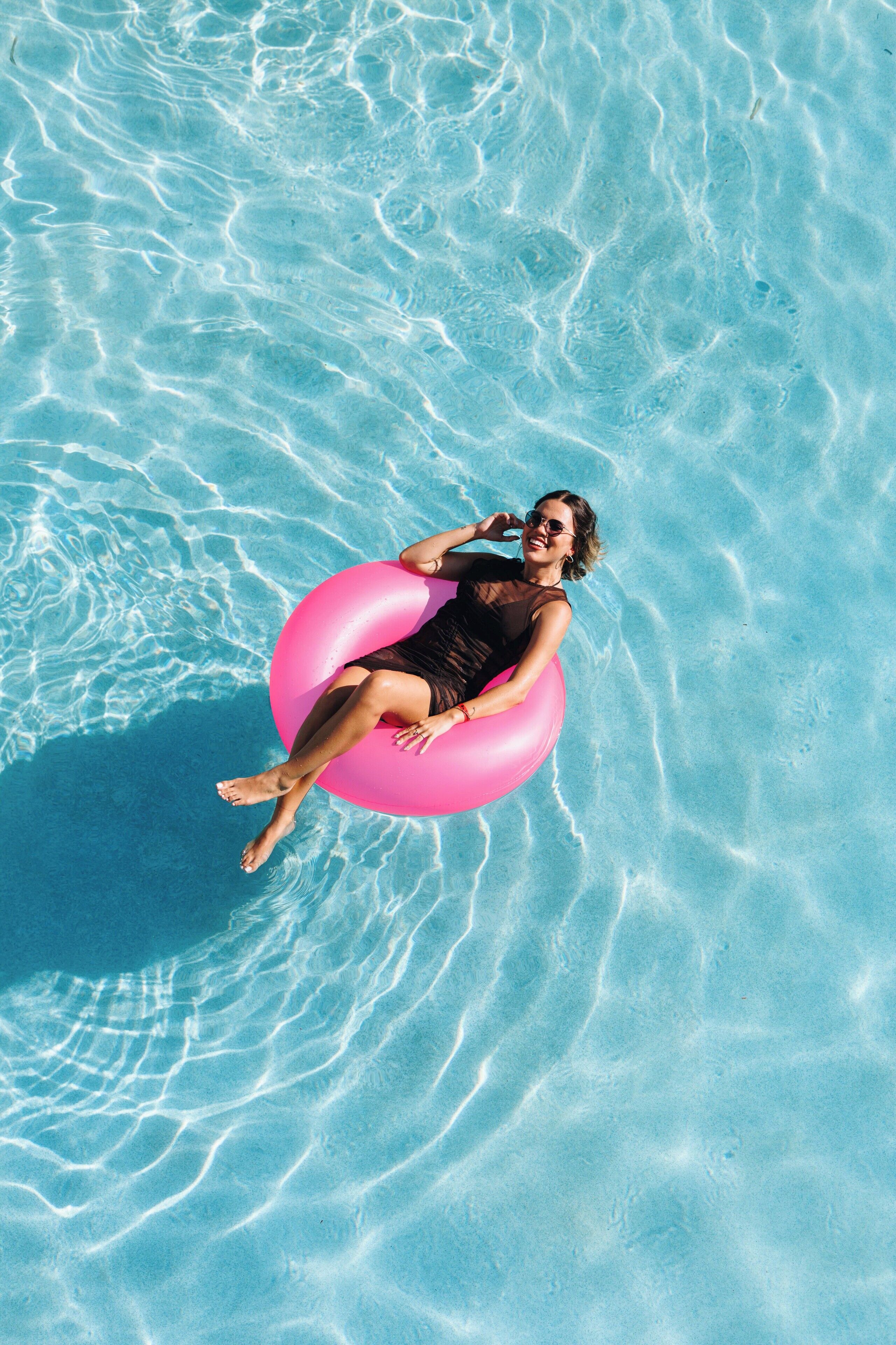 Une personne flotte sur un matelas gonflable rose dans une piscine à l’eau cristalline.