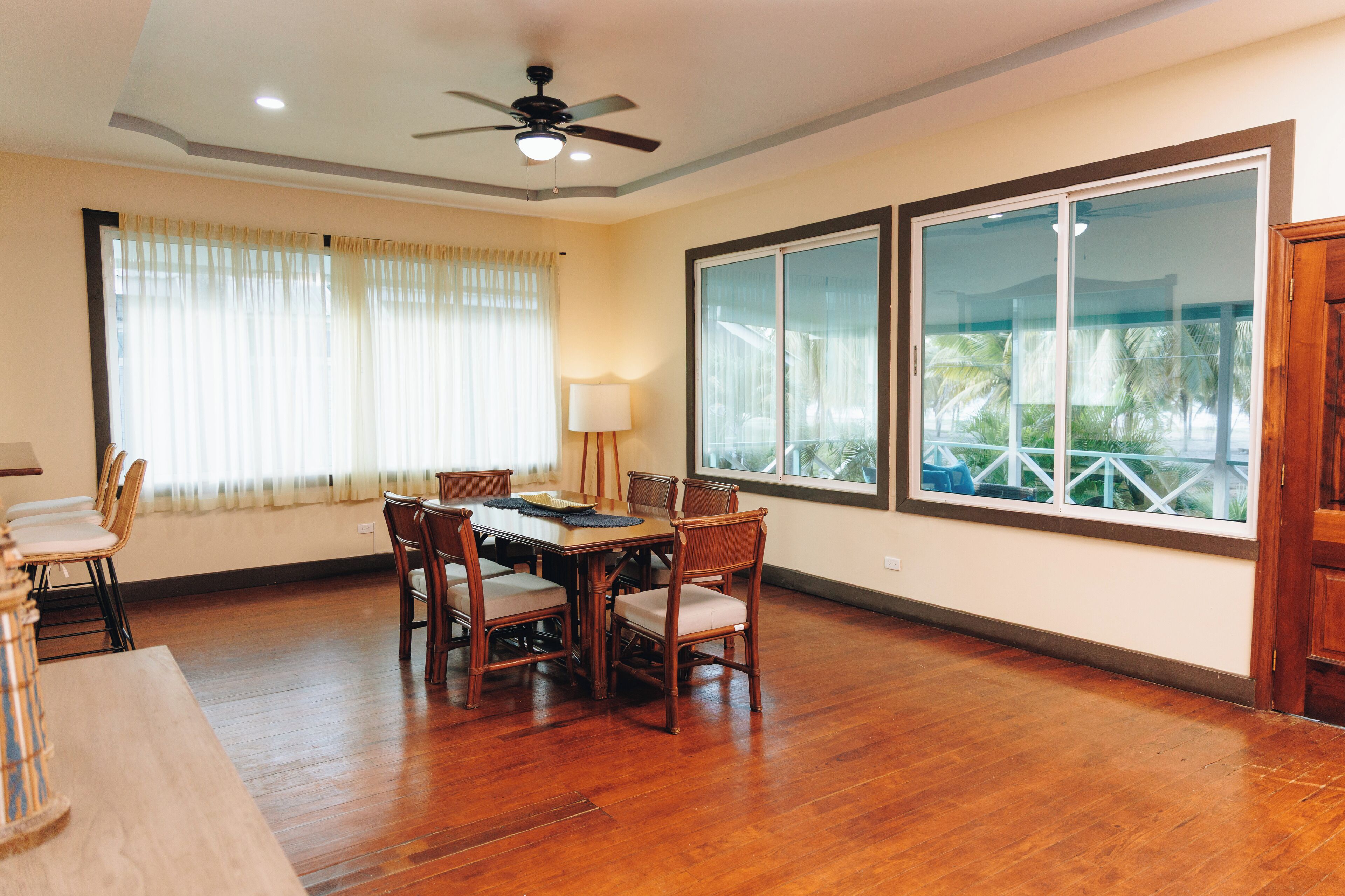 A dining area with a wooden table and chairs, a ceiling fan, and large windows with curtains.