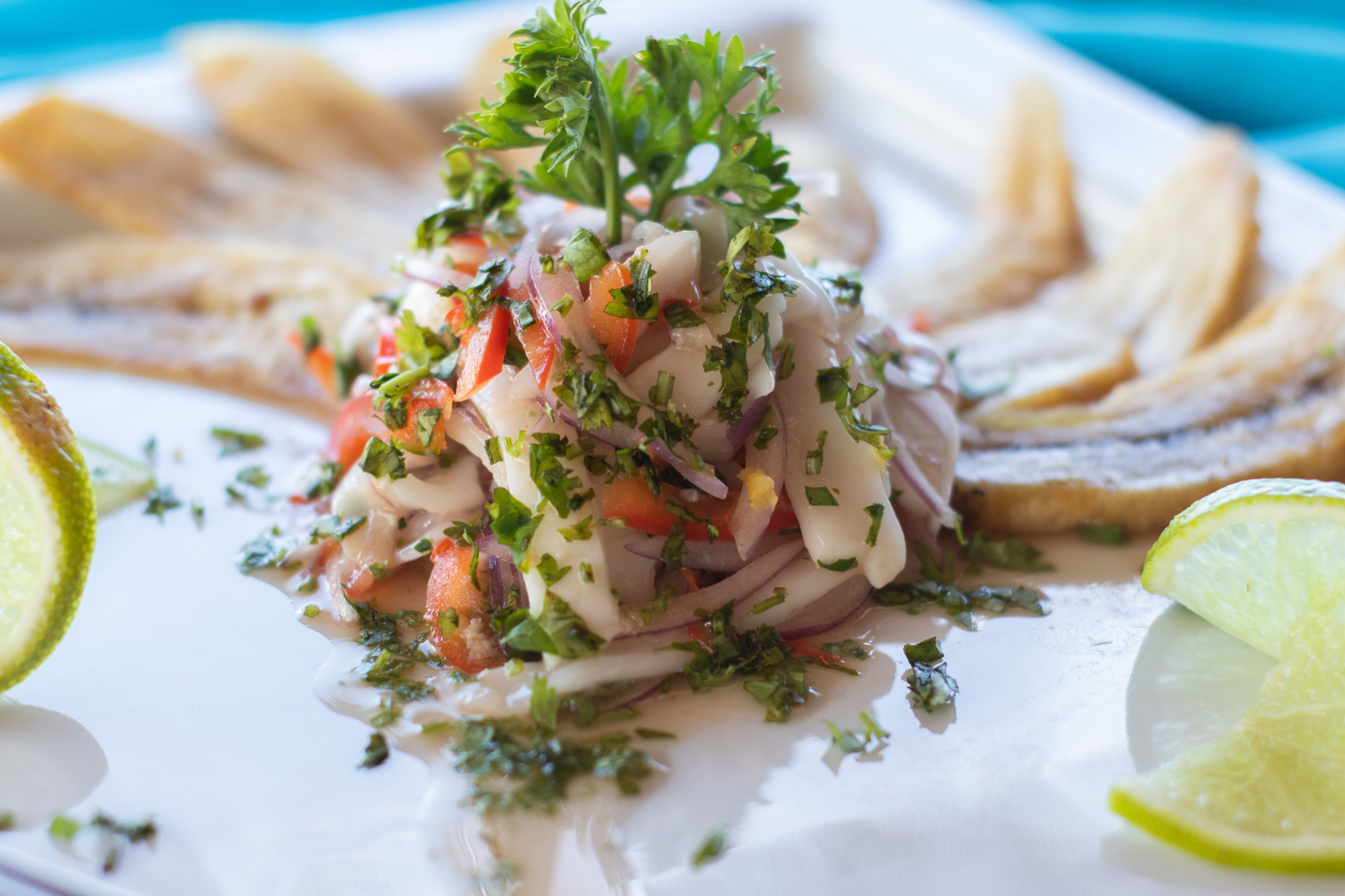 A plate of ceviche with lime wedges and parsley garnish.