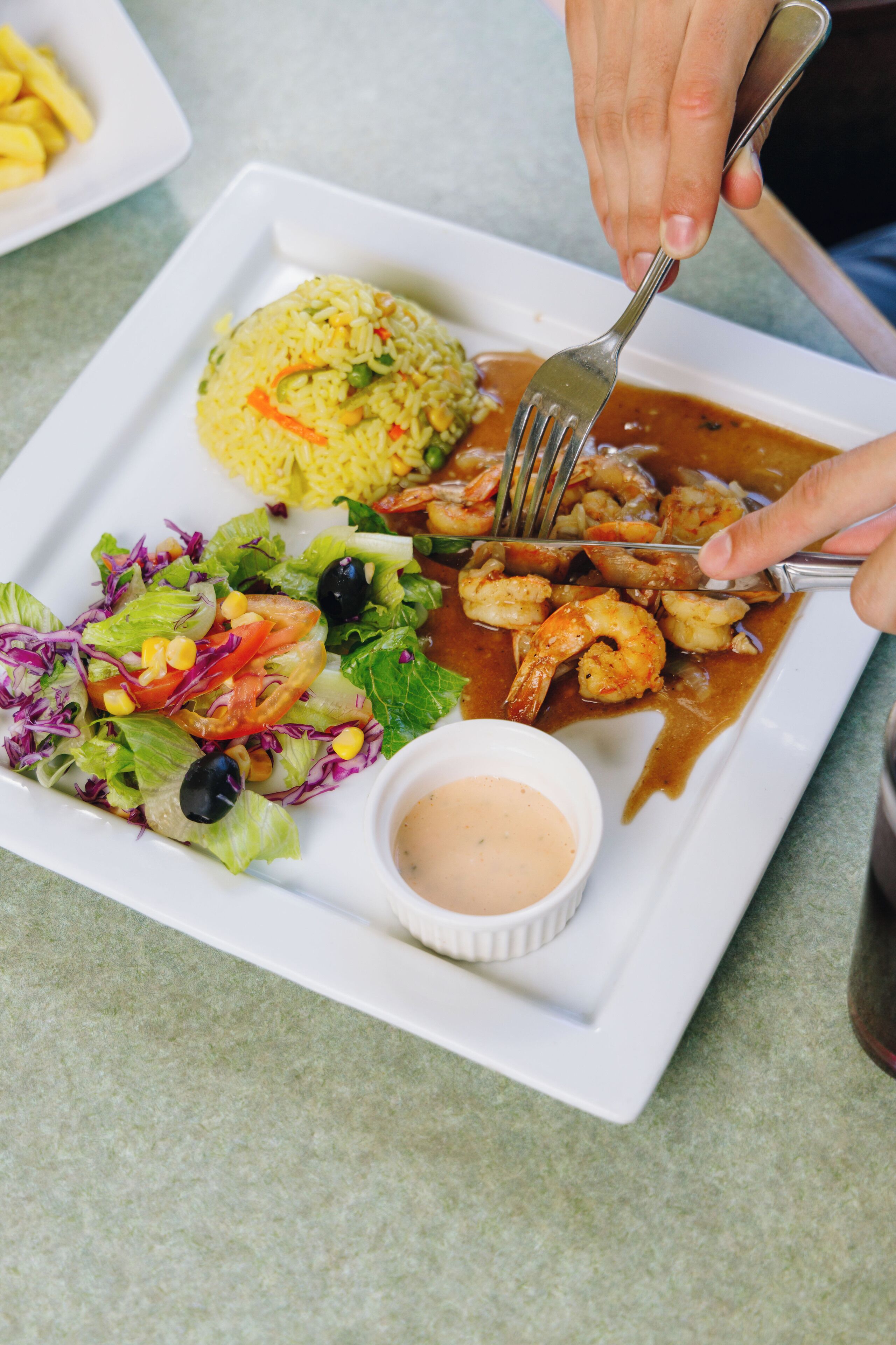 A plate of food with rice, shrimp, salad, and a dipping sauce.