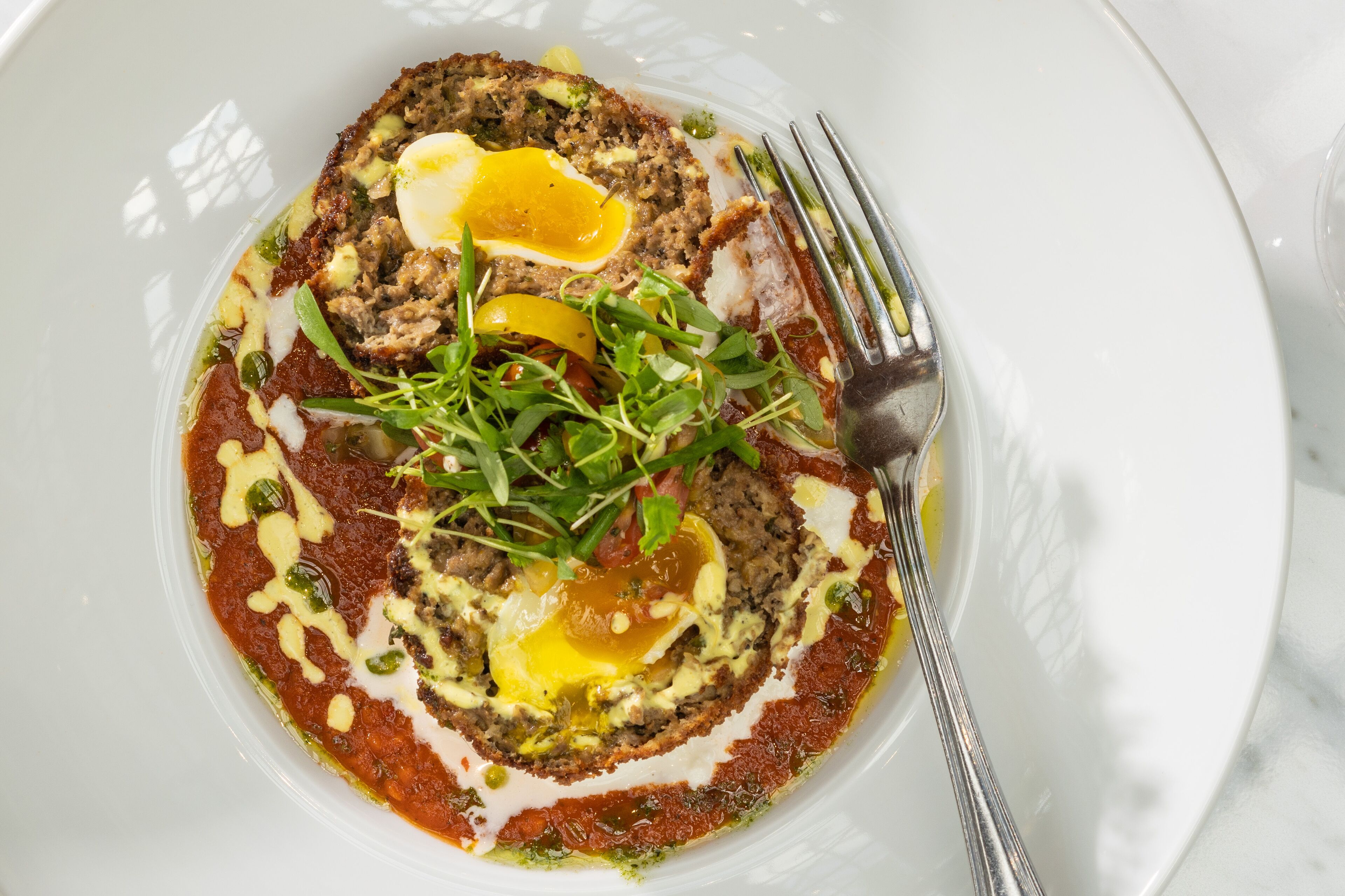 A white plate with a rolled meat dish, egg, greens, and sauce.
