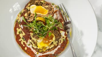 A white plate with a rolled meat dish, egg, greens, and sauce.