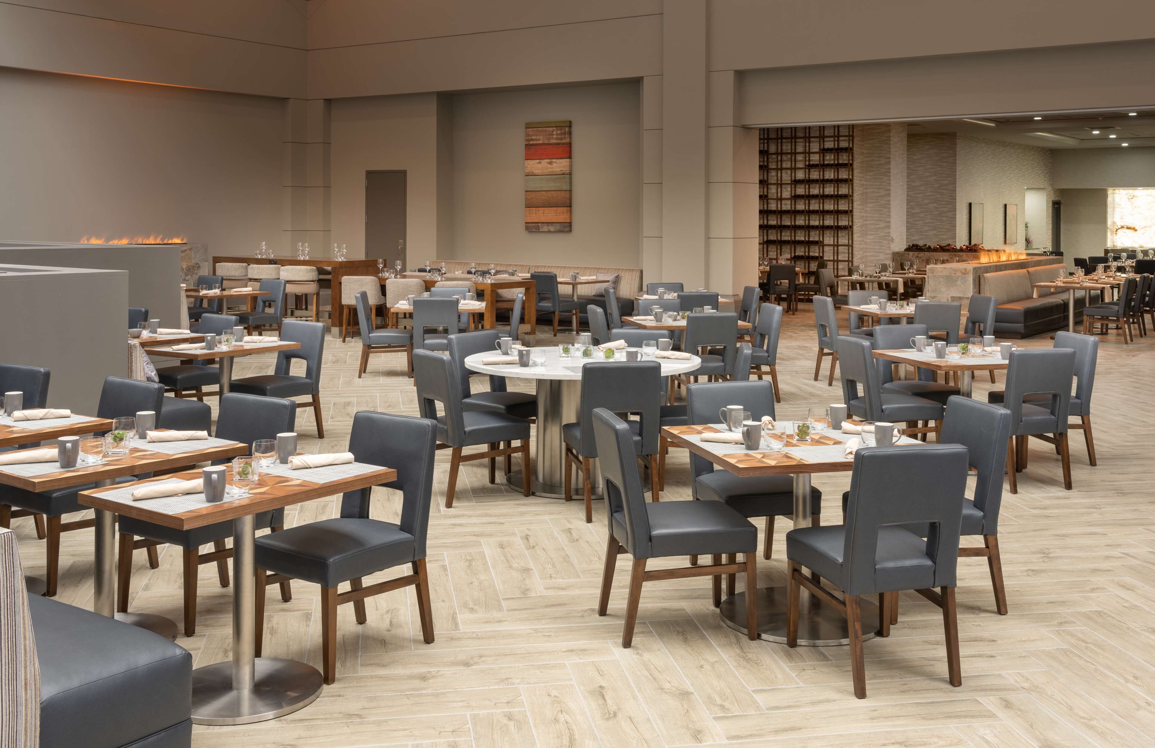 A spacious dining area with multiple tables and chairs, a fireplace, and a bookshelf in the background.