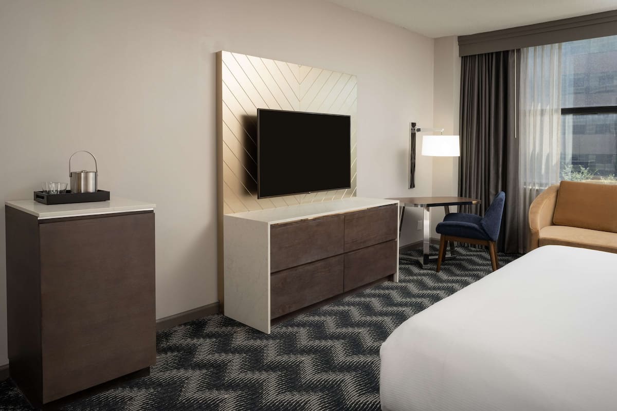 A hotel room with a flat-screen TV mounted on a wall, a desk with a chair, a bed, and a sofa.