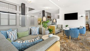 A modern living room with a grey sectional sofa, blue armchairs, a round coffee table, and a flat-screen TV mounted on the wall. - Hampton Inn Morgan Hill (Morgan Hill)