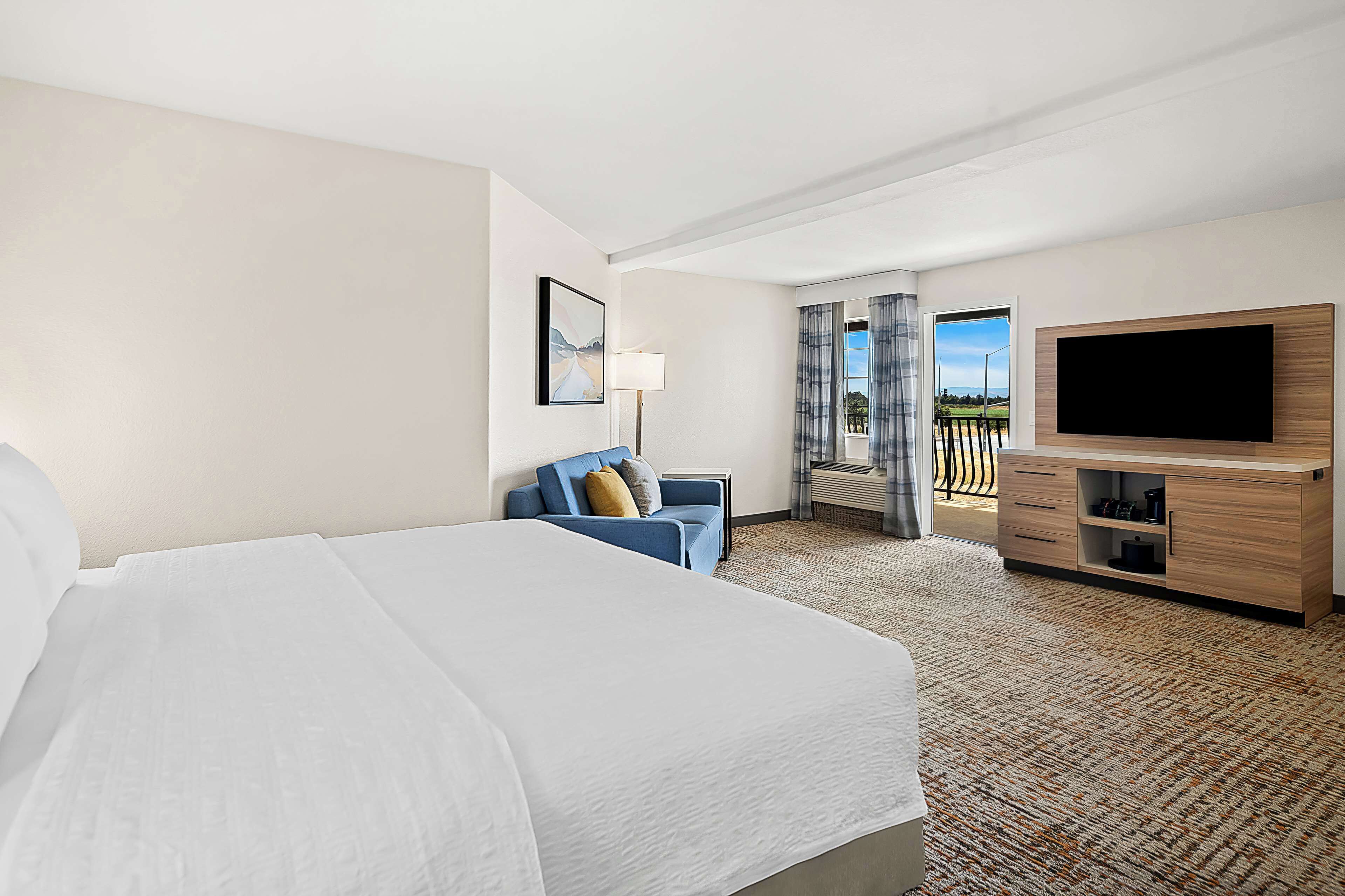 Een hotelkamer met een groot bed, een televisie, een bank en uitzicht op de omgeving.