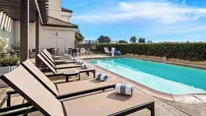 A pool area with lounge chairs and a small table, a tiled roof, and a clear blue sky.