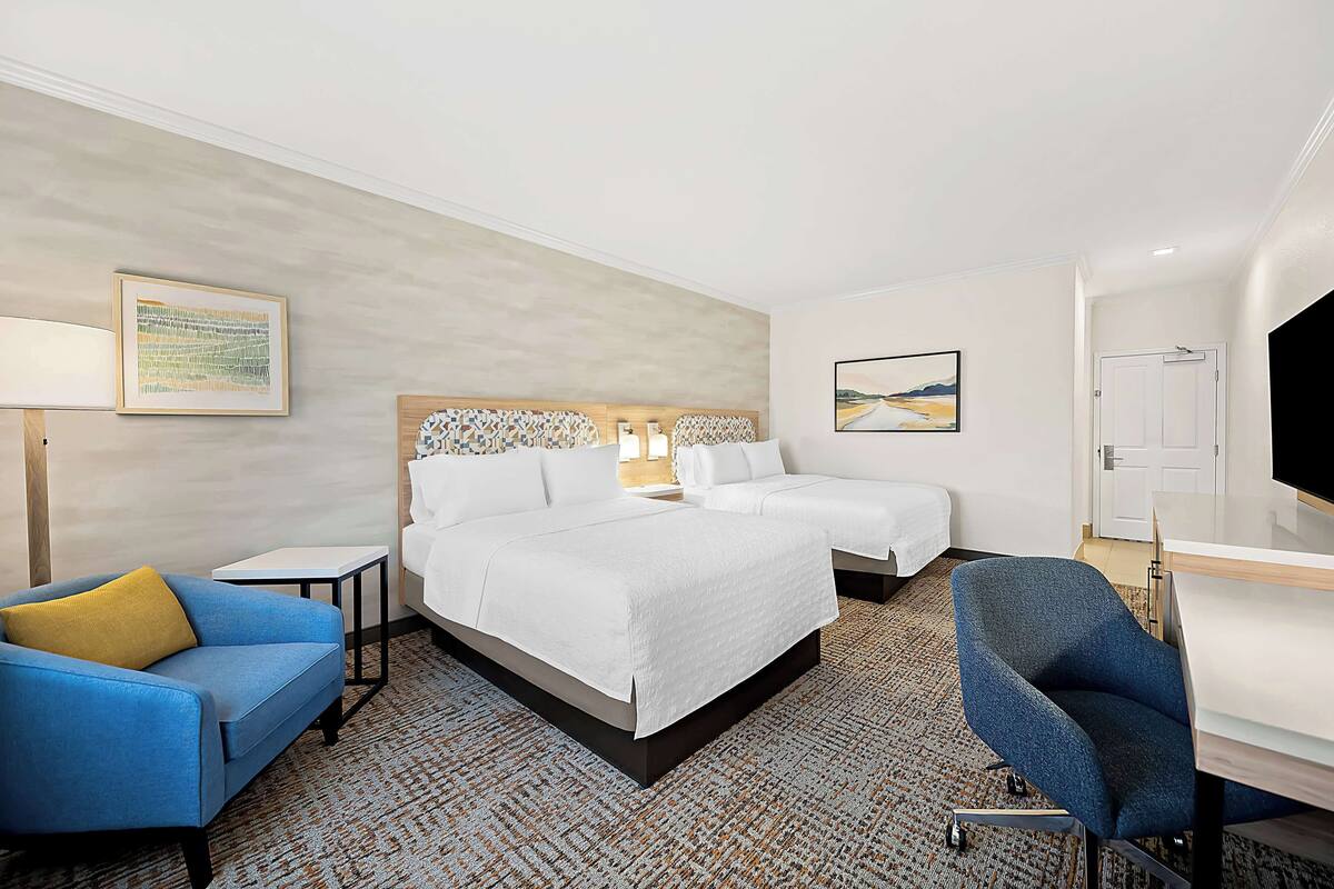 A hotel room with two beds, a desk, a chair, a sofa, and a TV.