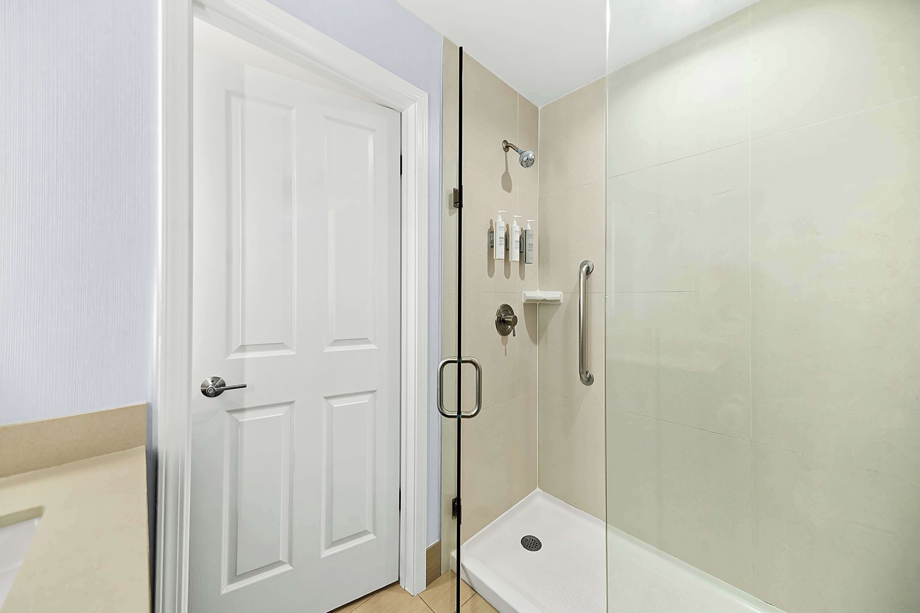 Un baño con puerta blanca, ducha con mampara de vidrio y artículos de aseo en un estante.