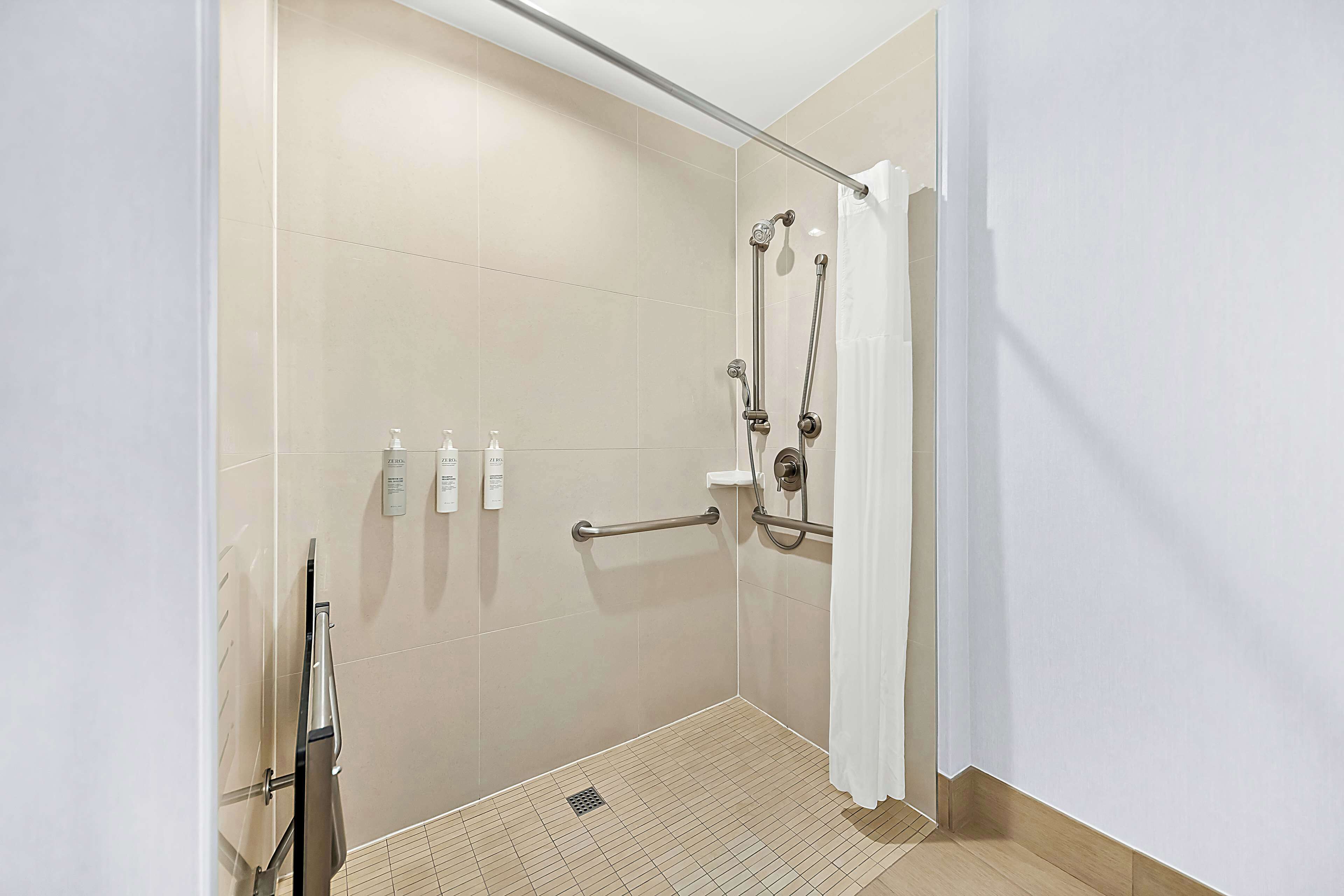 A modern bathroom with a walk-in shower, grab bars, and a hand dryer.