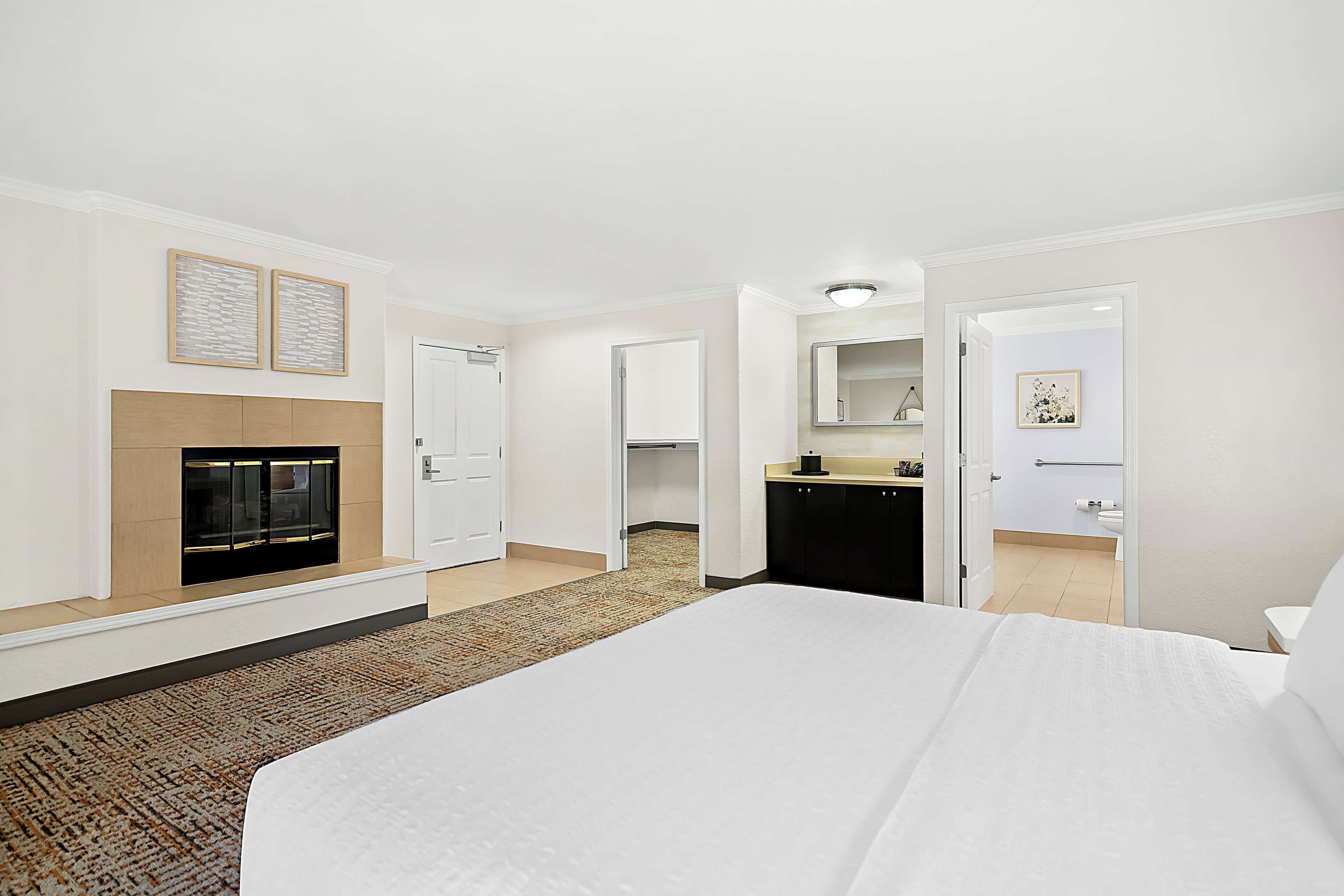 A hotel room with a large bed, a fireplace, a kitchen area, and a bathroom visible through an open door.